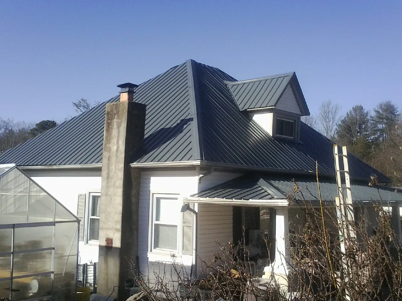 Dark blue standing seam metal roof on a white farmhouse with dormer — Slate & Tile Roof Repair by Roofing Brothers in Edgeley