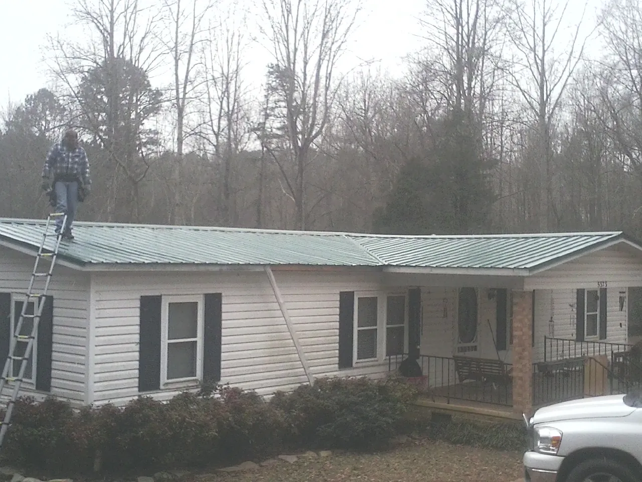 Worker on a ladder beside a new green metal roof on a ranch home in Edgeley