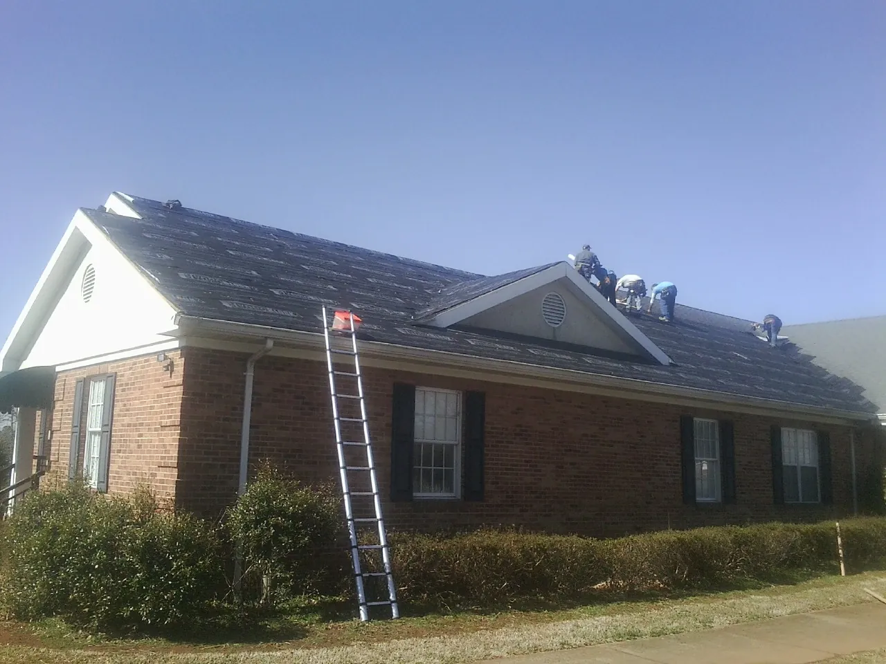 Crew tearing shingles off a brick ranch roof with a ladder set — Emergency Roof Repair work by our crew in Edgeley