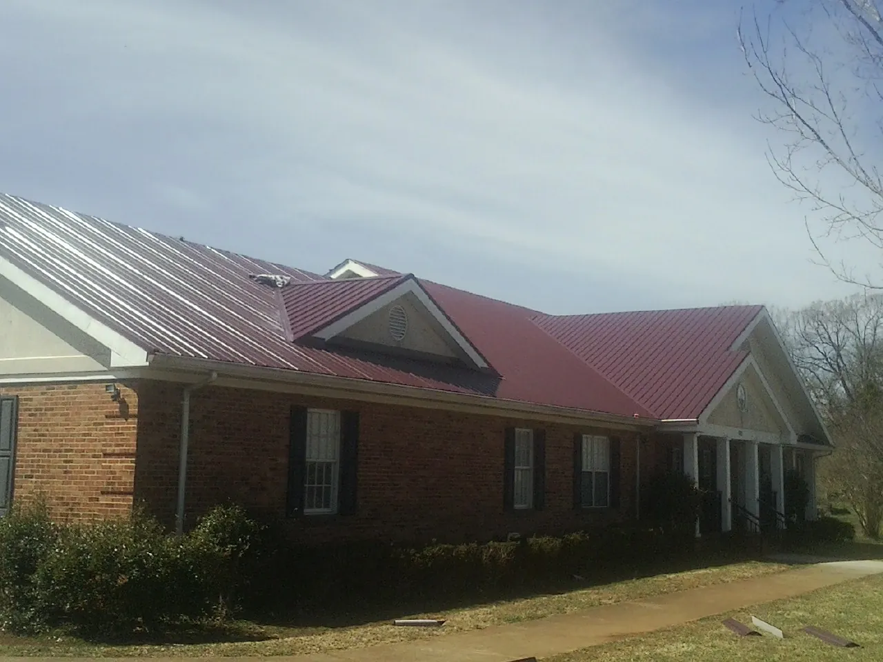 Red metal roof with gabled entries on a long brick building, from a Hail Damage Roof Repair job in Edgeley