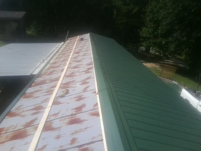 Old rusted panels beside newly installed green metal roofing — Wind Damage Roof Repair by Roofing Brothers in Edgeley