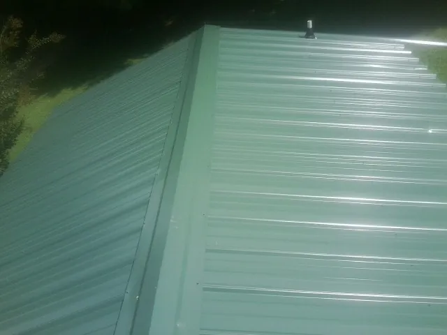 New green metal panels meeting at the ridge of a roof — Flat Roof Repair work by our crew in Edgeley