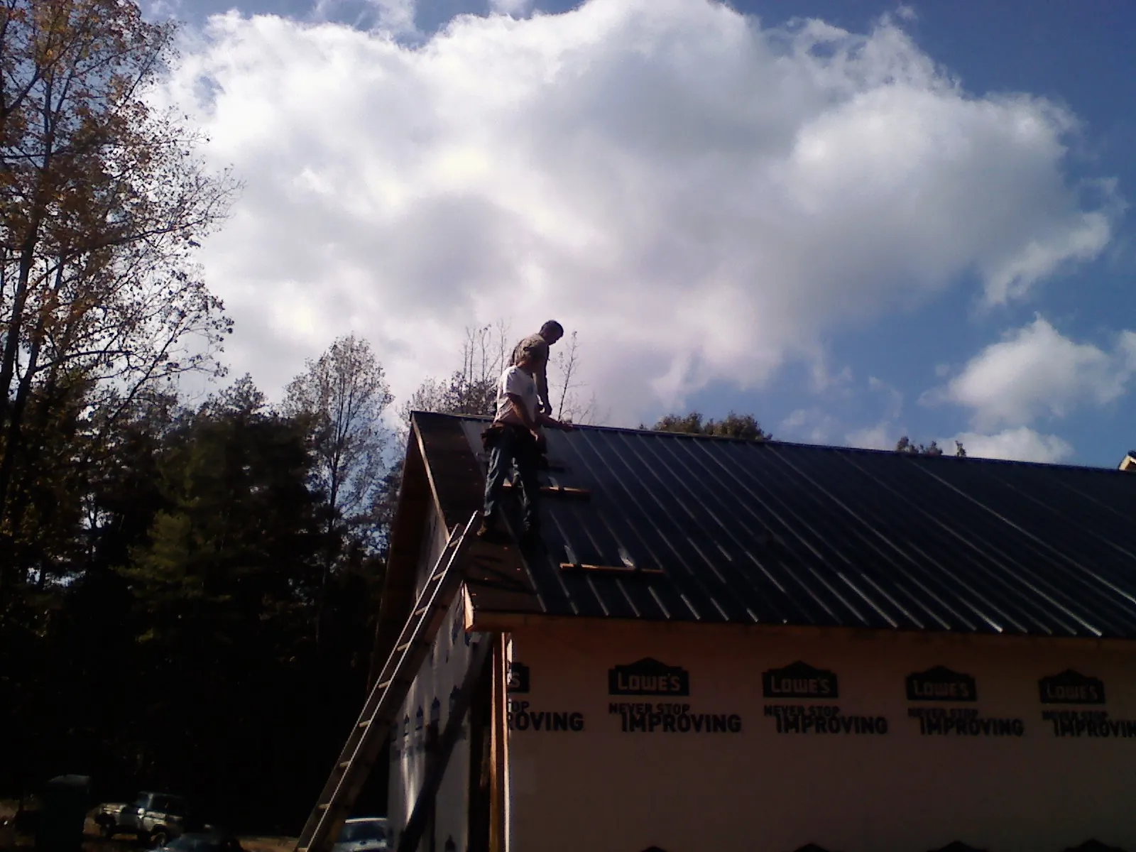 Roofer fastening dark metal panels high against a cloudy sky, from a Roof Inspection job in Edgeley